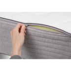 Hand öffnet Reißverschluss einer Bico Basics Matratze 90x200 cm und gibt Blick auf grünen Schaumstoffkern frei
