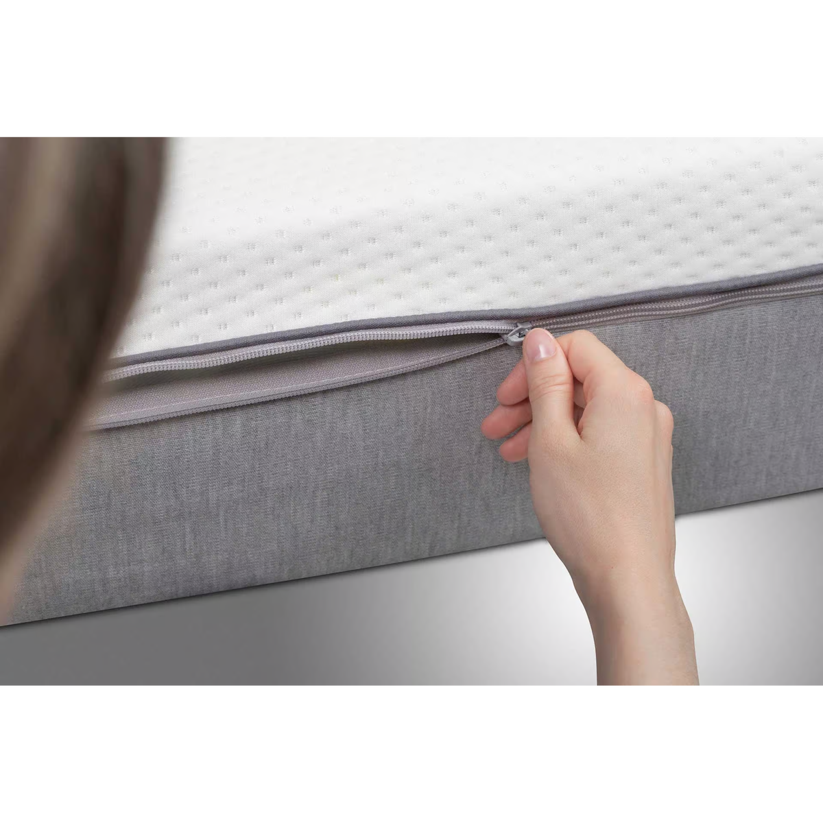 Frau öffnet Reißverschluss des abnehmbaren Bezugs der Bico Matratze Basics 90x200 cm in Grau/Weiß